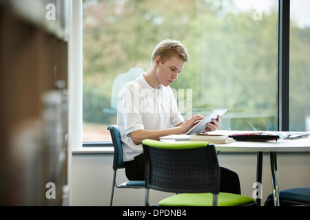 Teenage boy using digital tablet in library Banque D'Images