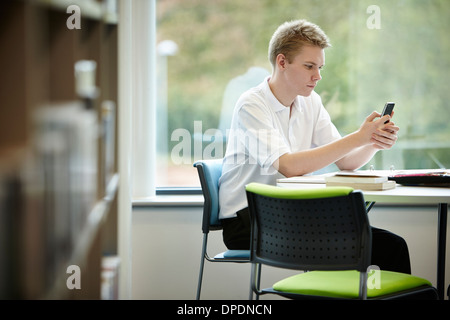 Teenage boy using cell phone in library Banque D'Images