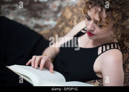 Portrait of young woman reclining and reading book Banque D'Images