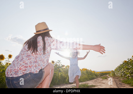 Fille courir à travers champ pour mère à bras ouverts Banque D'Images