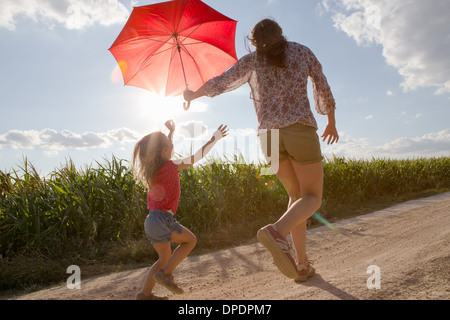 Mère et fille marchant à travers l'exécution de champ parapluie rouge Banque D'Images