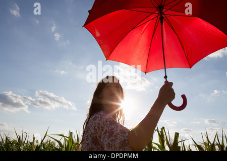 Femme debout tenant parapluie rouge Banque D'Images