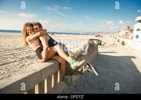 Young couple sitting on wall at San Diego beach Banque D'Images