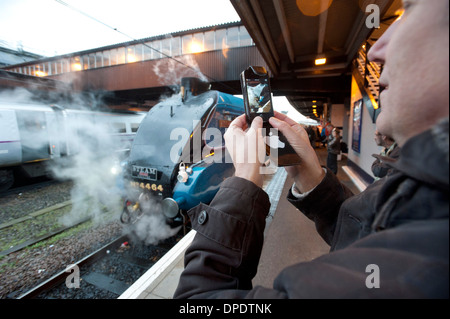 Un passionné de chemin de fer utilise son Apple iPhone pour photographier un London North Eastern Railway (LNER) Catégorie A4 locomotive à vapeur. Banque D'Images