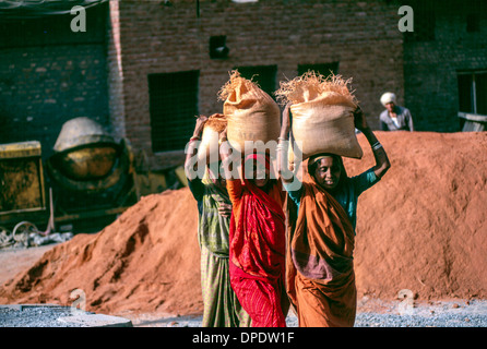 Trois jeunes femmes de basse caste portant des saris aux couleurs vives transporter des sacs de sable sur un chantier à Delhi Inde Banque D'Images