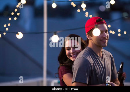 Jeune couple hugging at rooftop barbecue Banque D'Images