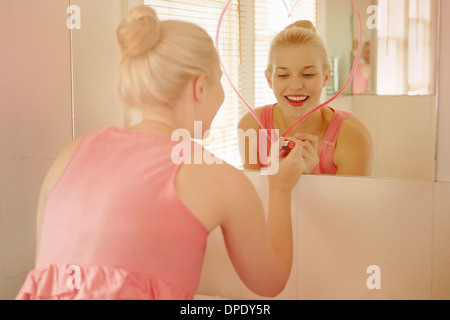 Jeune femme dans la salle de bains dimensions forme de cœur sur le rouge à lèvres avec miroir Banque D'Images