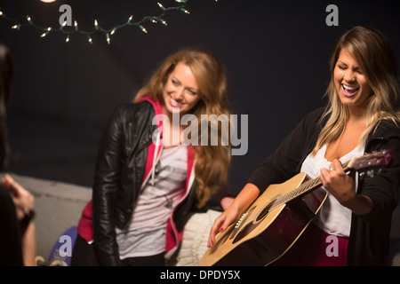 Female friends enjoying guitar music at rooftop party Banque D'Images