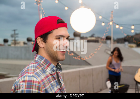 Jeune homme de baseball cap at rooftop barbecue Banque D'Images