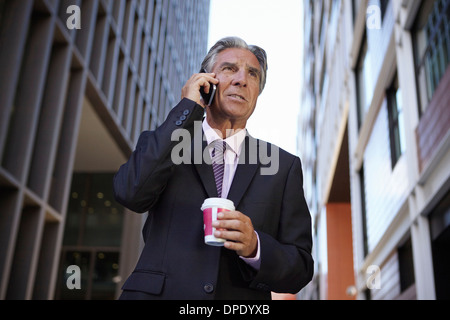 Businessman holding smartphone et boisson chaude, rendant phonecall Banque D'Images