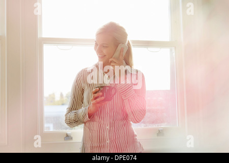 Young woman on phonecall, holding hot drink Banque D'Images