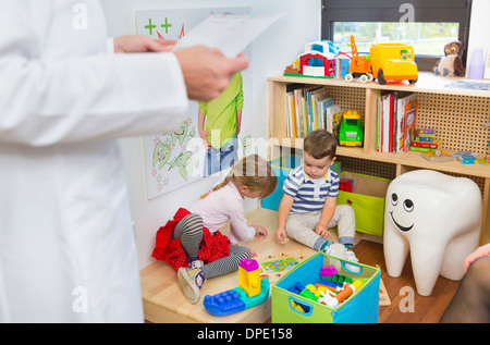 Enfants jouant sur le plancher, dentiste en premier plan Banque D'Images