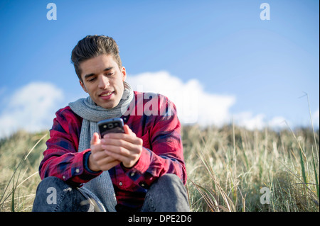 Young man sitting on grass using smartphone Banque D'Images