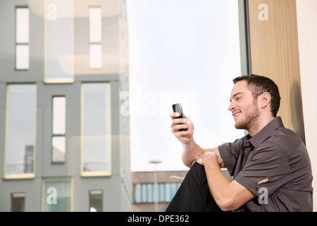 Businessman sitting on windowsill using smartphone Banque D'Images