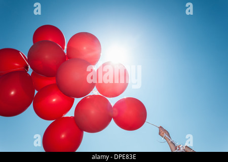 Hands holding bunch of red balloons against blue sky Banque D'Images