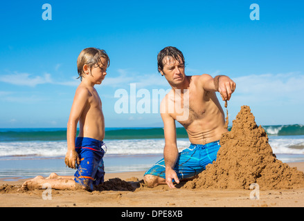 Père et fils jouent ensemble dans le sable on tropical beach, château de sable de construction Banque D'Images