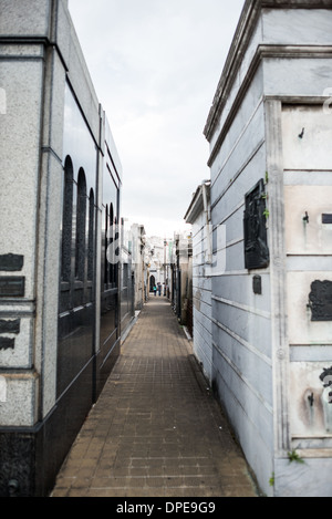 BUENOS AIRES, Argentine — Un passage étroit entre les mausolées du cimetière de Recoleta (Cementerio de la Recoleta) illustre l'agencement de style urbain du cimetière. Ces couloirs intimes, conçus pour imiter les rues de la ville, créent une grille organisée reliant les tombes et monuments élaborés du cimetière. La proximité des mausolées crée des perspectives spectaculaires typiques de ce cimetière historique. Banque D'Images