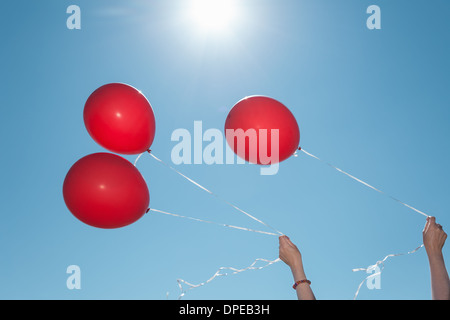 Mains tenant trois ballons rouges sur fond de ciel bleu Banque D'Images