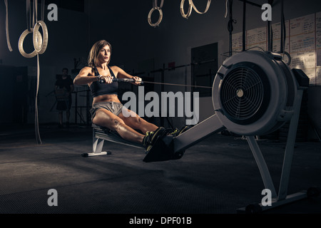 Femme à l'aide d'une machine à ramer en salle de sport Banque D'Images