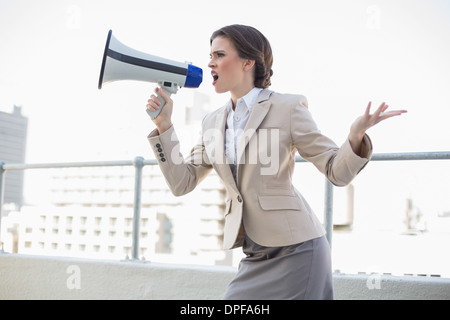 Élégant brown haired woman furieuse criant dans un mégaphone Banque D'Images