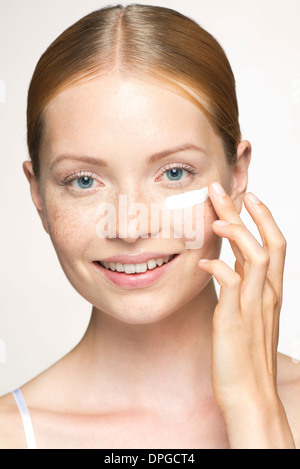 Young woman applying moisturizer under eye Banque D'Images