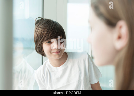 Teenage boy leaning against window, smiling at girl en premier plan Banque D'Images