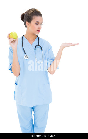 Jolie infirmière brune en bleu frotte holding a green apple Banque D'Images