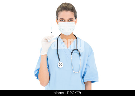 Brun mignon infirmière dans scrubs bleu portant un masque de protection et la tenue d'une seringue Banque D'Images