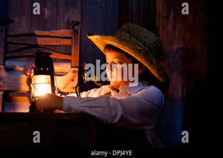 Un petit garçon fermier dans la grange avec une lampe à huile Banque D'Images