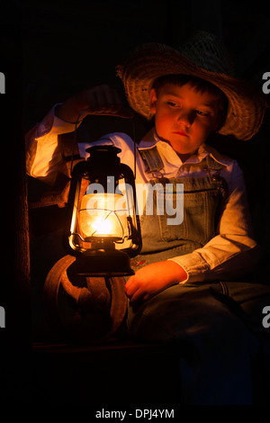 Un petit garçon fermier dans la grange avec une lampe à huile Banque D'Images