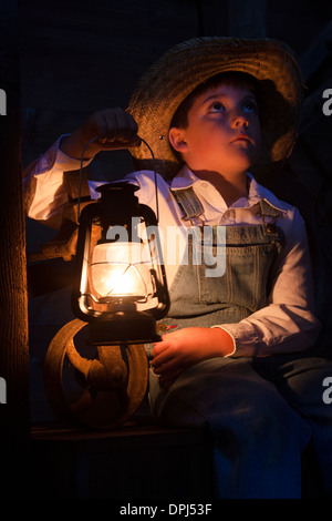 Un petit garçon fermier dans la grange avec une lampe à huile Banque D'Images