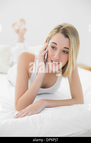 Gorgeous blonde woman lying on her bed tout en téléphonant au Banque D'Images