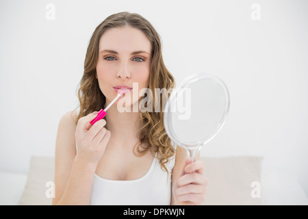 Jeune femme à l'aide d'un brillant à lèvres et à la recherche dans l'appareil photo Banque D'Images