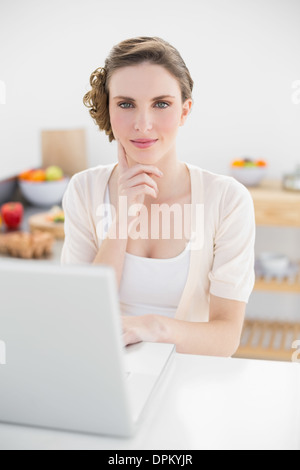 Penser Pretty woman sitting in kitchen en utilisant son ordinateur portable Banque D'Images