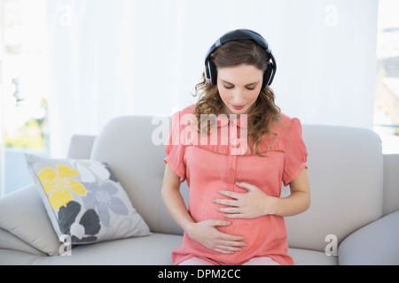 Calme belle femme enceinte se détendre en écoutant de la musique dans la salle de séjour Banque D'Images