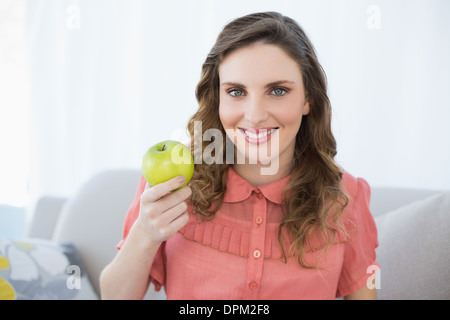 Smiling pregnant woman presenting green apple assis dans la salle de séjour Banque D'Images