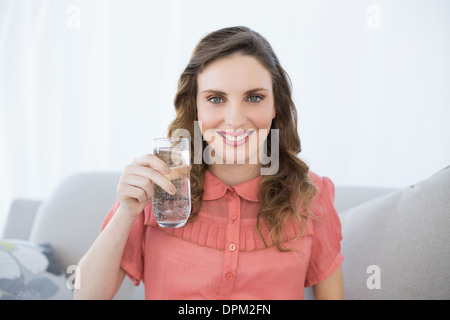 Jolie femme enceinte montrant verre d'eau sitting on couch Banque D'Images