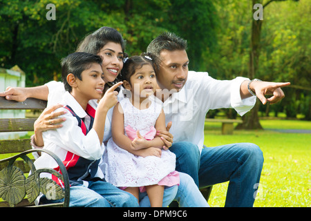 Heureux famille indienne à l'extérieur parc. Portrait sincère des parents et des enfants s'amusant à garden park. Doigts dirigés à l'écart. Banque D'Images