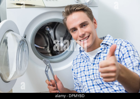 La réparation d'un lave-linge tandis que technicien gesturing Thumbs up Banque D'Images
