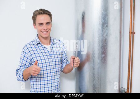 Technician gesturing Thumbs up par chauffe-eau chaude Banque D'Images