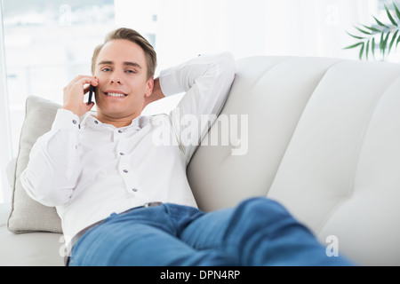 Jeune homme détendu using cellphone while lying on sofa Banque D'Images