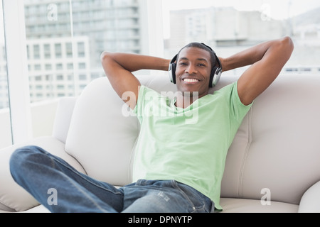 Jeune homme Afro détendue avec des écouteurs sitting on sofa Banque D'Images