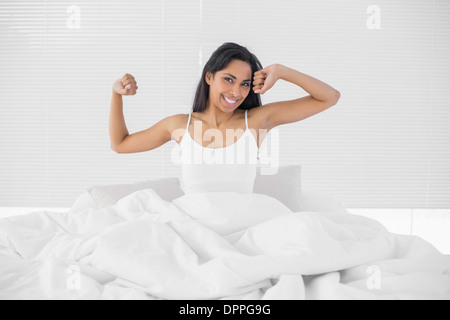 Jolie femme souriante qui s'assis sur son lit Banque D'Images