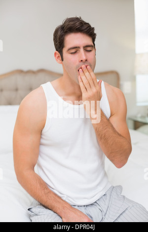 Jeune homme yawning in bed at home Banque D'Images