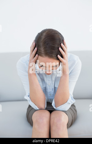 Inquiète bien habillé femme avec la tête dans les mains sur le canapé Banque D'Images