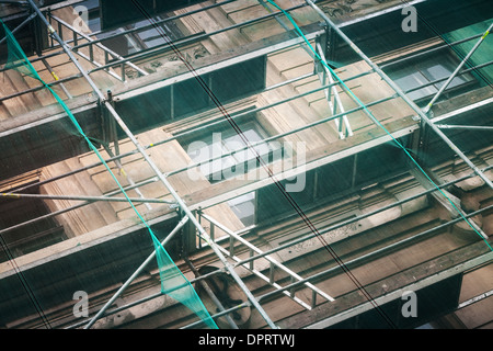 Vieille façade de l'immeuble en construction avec des mailles de protection vert Banque D'Images