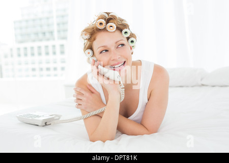Belle femme dans les bigoudis en utilisant phone in bed Banque D'Images