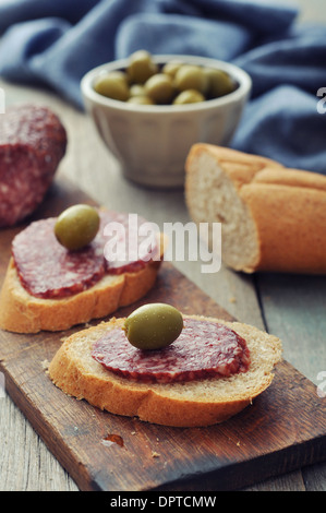 Canape avec olives et salami sur planche à découper en bois libre Banque D'Images