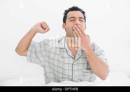 Jeune homme yawning in bed Banque D'Images