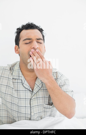 Jeune homme yawning in bed Banque D'Images